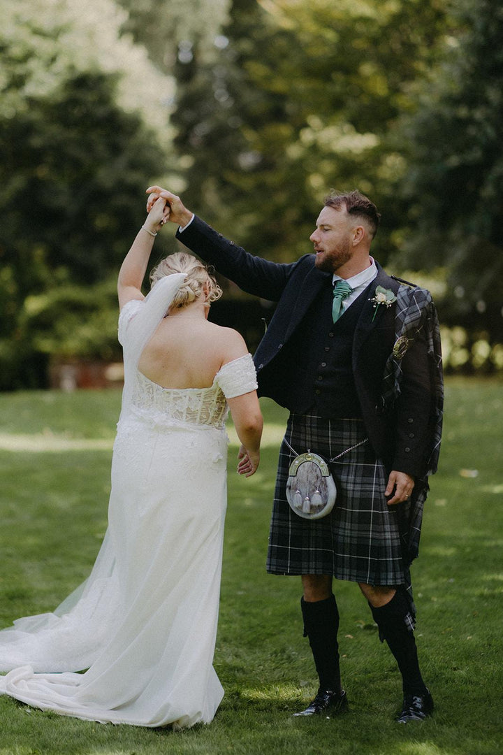 Real bride wearing the Celtic Pearl fitted crepe wedding gown with groom in a Scottish kilt